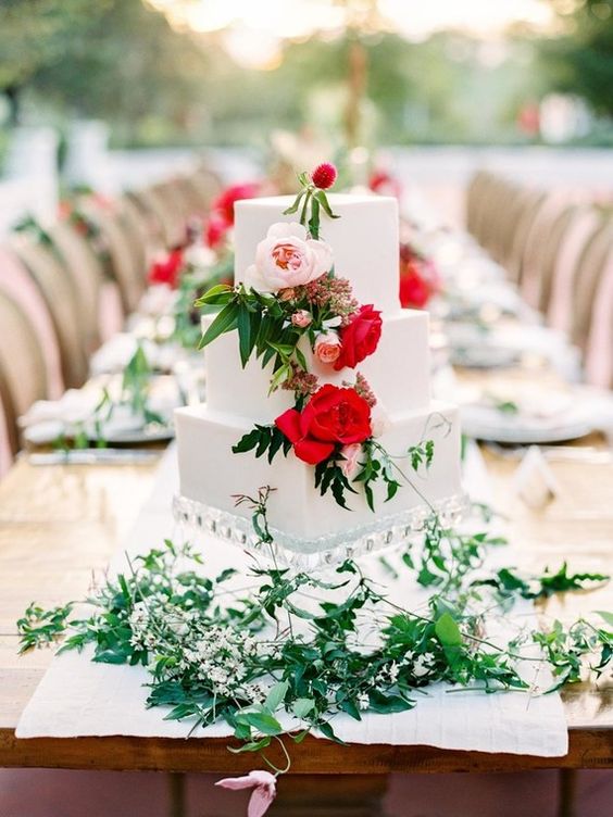 white wedding cake with red flowers and table decorations for rustic red and white wedding